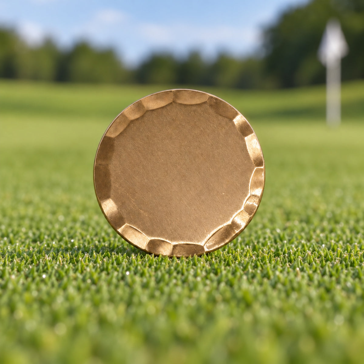 Blank 38 mm bronze golf ball marker with a bevelled edge, standing on a putting green