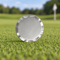 Blank 38 mm silver golf ball marker with a bevelled edge, standing on a putting green