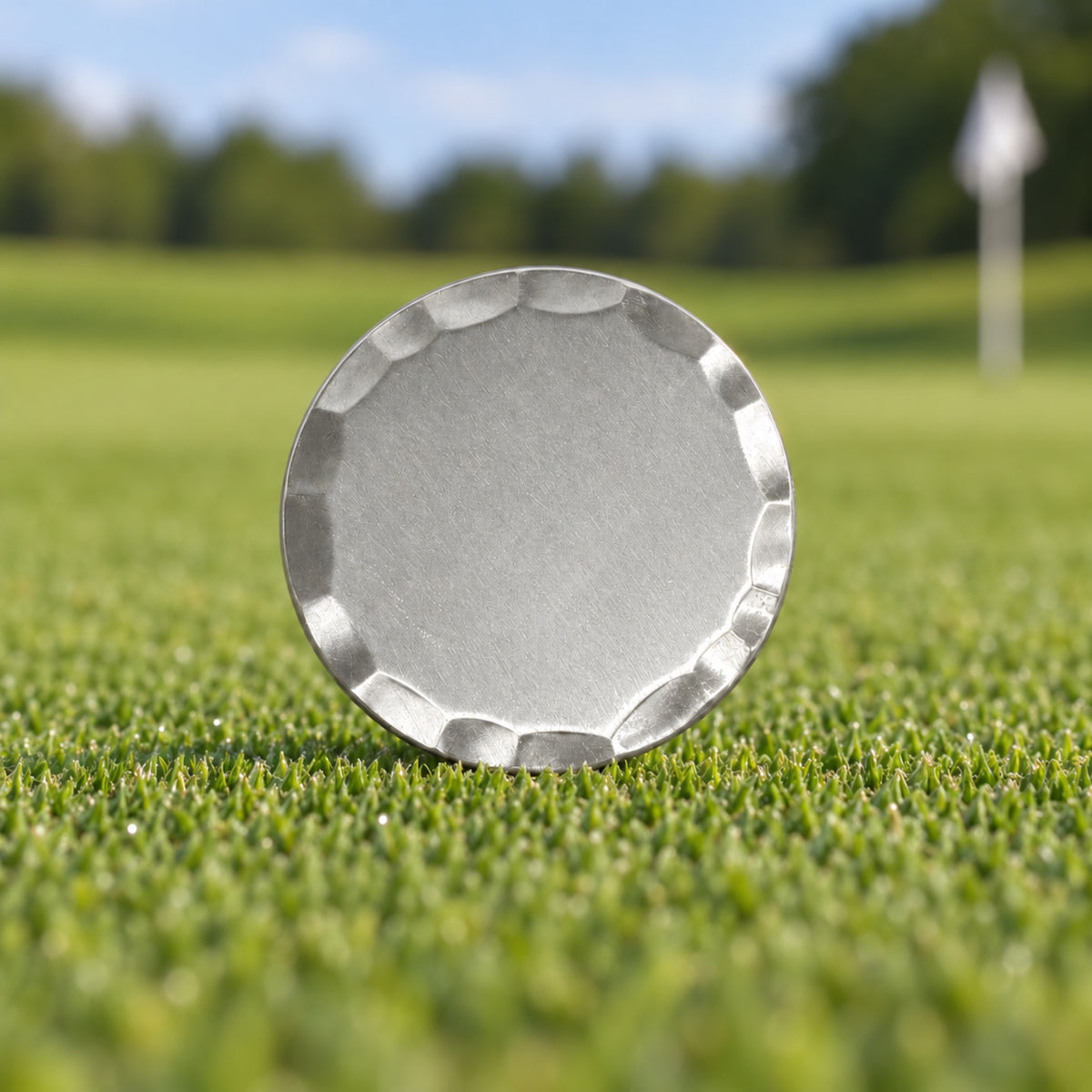 Blank 38 mm silver golf ball marker with a bevelled edge, standing on a putting green